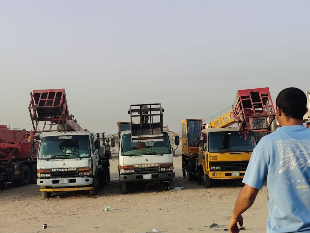 ساحة معدات فيها ثلاث رافعات سلة مركبة على شاحنات ورافعة شوكية وكرين في الخلفية