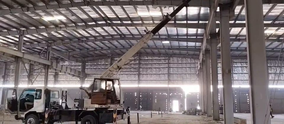 Video of lifting work inside a large steel warehouse using a boom lift and a truck-mounted crane