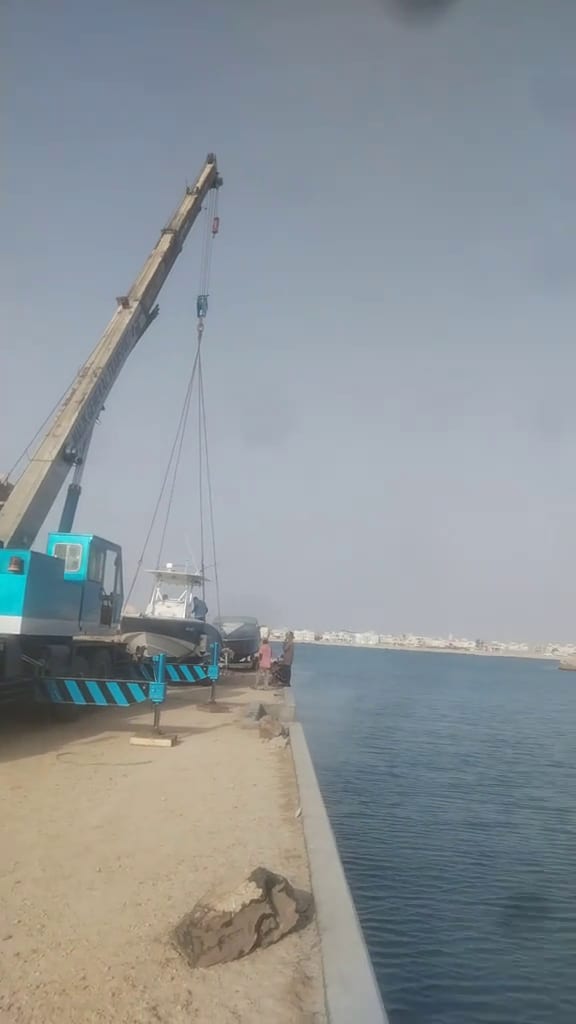 فيديو لكرين متحرك أزرق على رصيف بحري ينزل قاربًا معلقًا بسلنجين إلى الماء